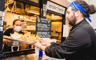 Server handing tray of vegetarian street food to customer at South Lake Union eatery.