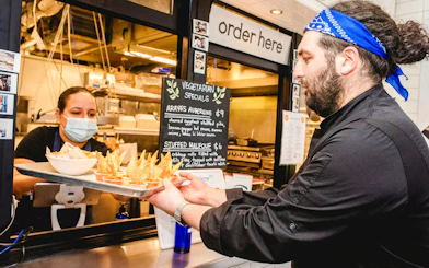 Server handing tray of vegetarian street food to customer at South Lake Union eatery.