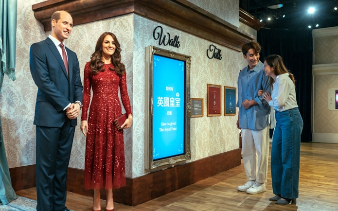 Wax figures of a royal couple at Madame Tussauds Hong Kong with visitors observing.