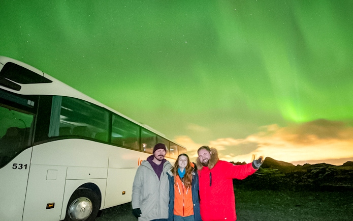 Guests on a Northern Lights sightseeing bus tour with aurora borealis in the background.