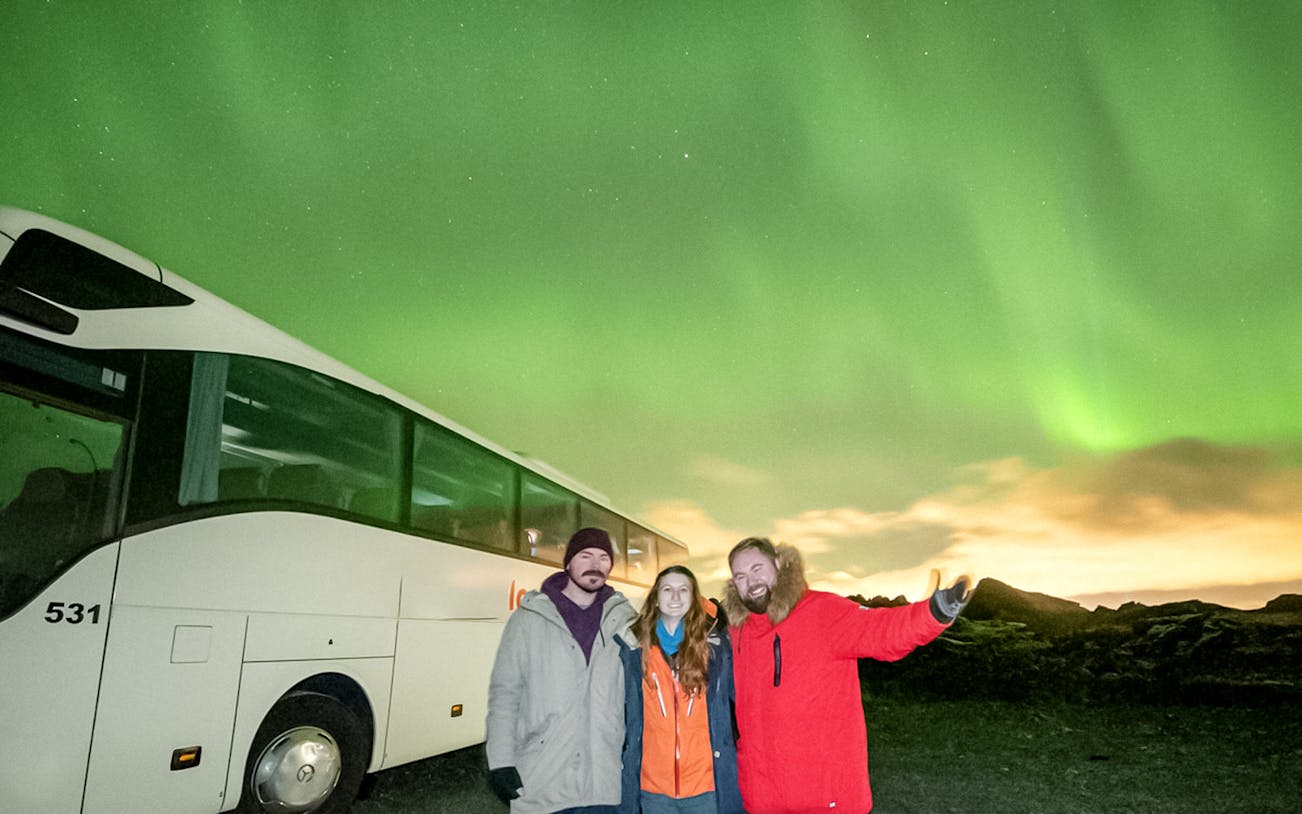 Guests on a Northern Lights sightseeing bus tour with aurora borealis in the background.