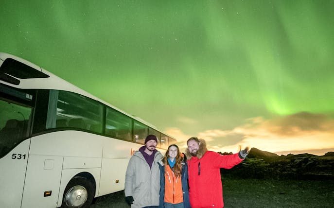 Guests on a Northern Lights sightseeing bus tour with aurora borealis in the background.