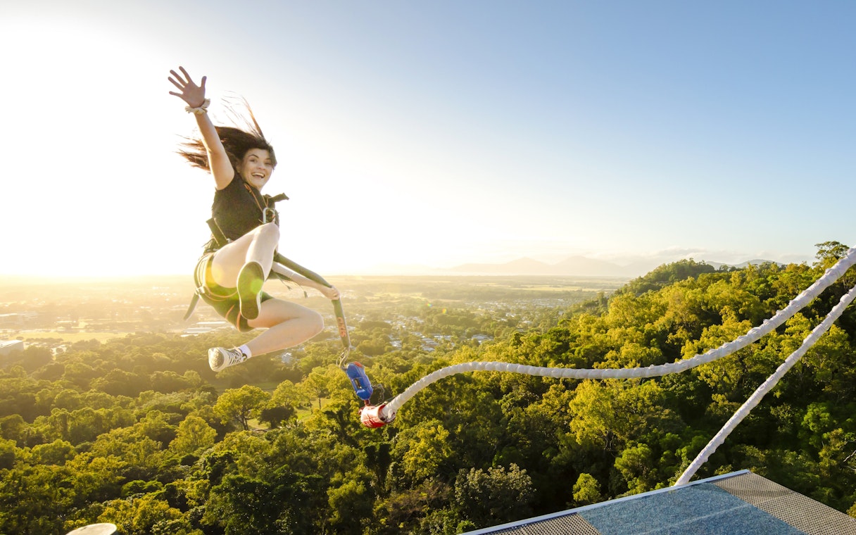 Person bungee jumping from a platform with a scenic view of lush landscape and mountains.