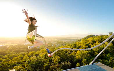 Person bungee jumping from a platform with a scenic view of lush landscape and mountains.