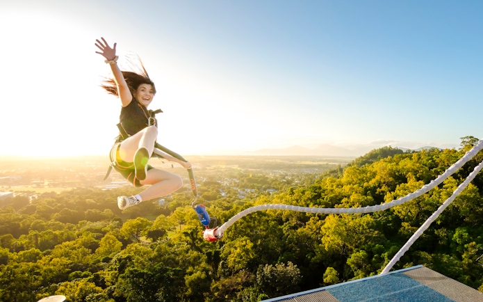 Person bungee jumping from a platform with a scenic view of lush landscape and mountains.
