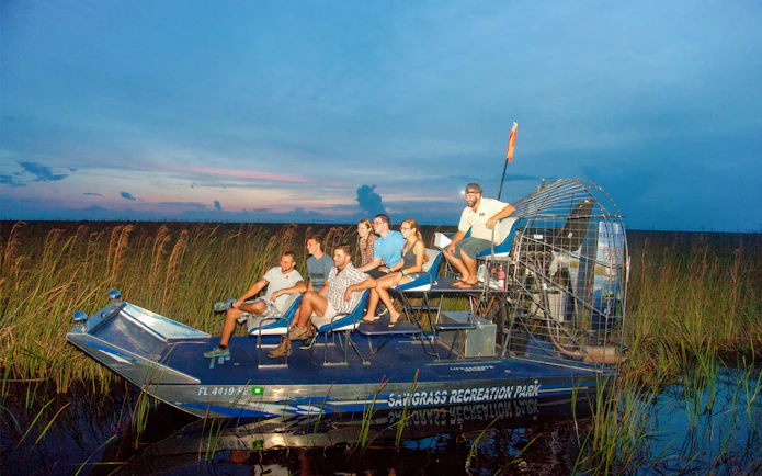 Group on an airboat during a night tour in the Everglades, surrounded by marshland.