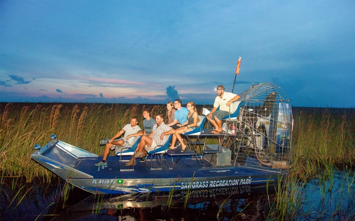 Group on an airboat during a night tour in the Everglades, surrounded by marshland.