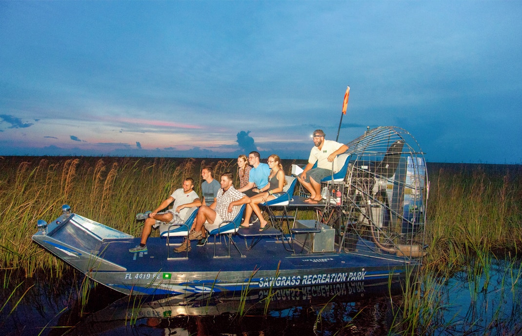 Group on an airboat during a night tour in the Everglades, surrounded by marshland.