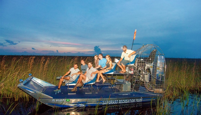 Group on an airboat during a night tour in the Everglades, surrounded by marshland.