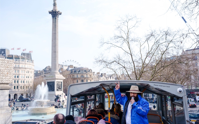 Open-top bus tour at Trafalgar Square, London with guide speaking.