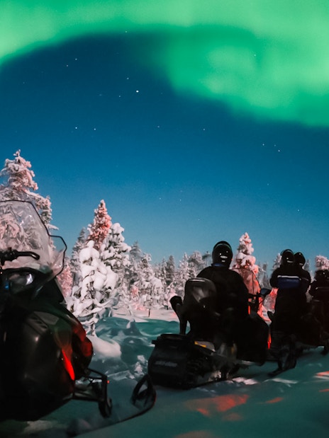 Snowmobile ride under Northern Lights in Levi, Finland.
