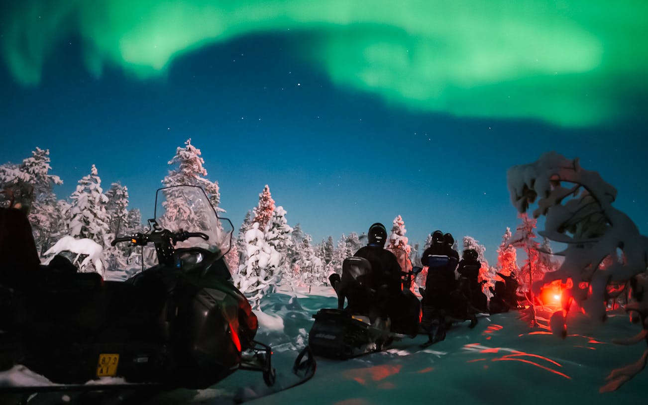 Snowmobile ride under Northern Lights in Levi, Finland.
