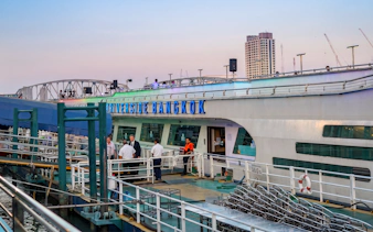 Riverside Bangkok cruise ship docked with people boarding in the evening.