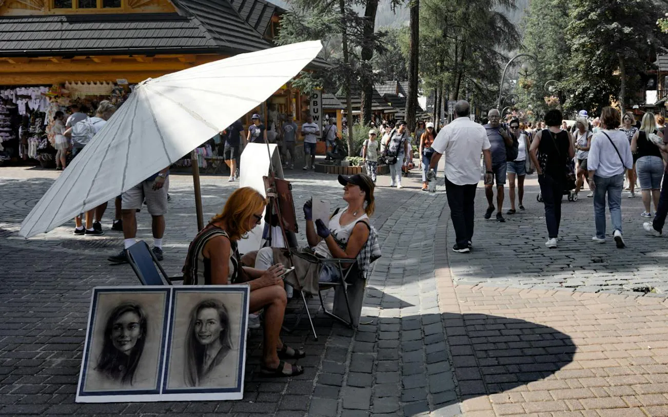 Street artist drawing portraits in Zakopane market, Poland, with tourists walking nearby.