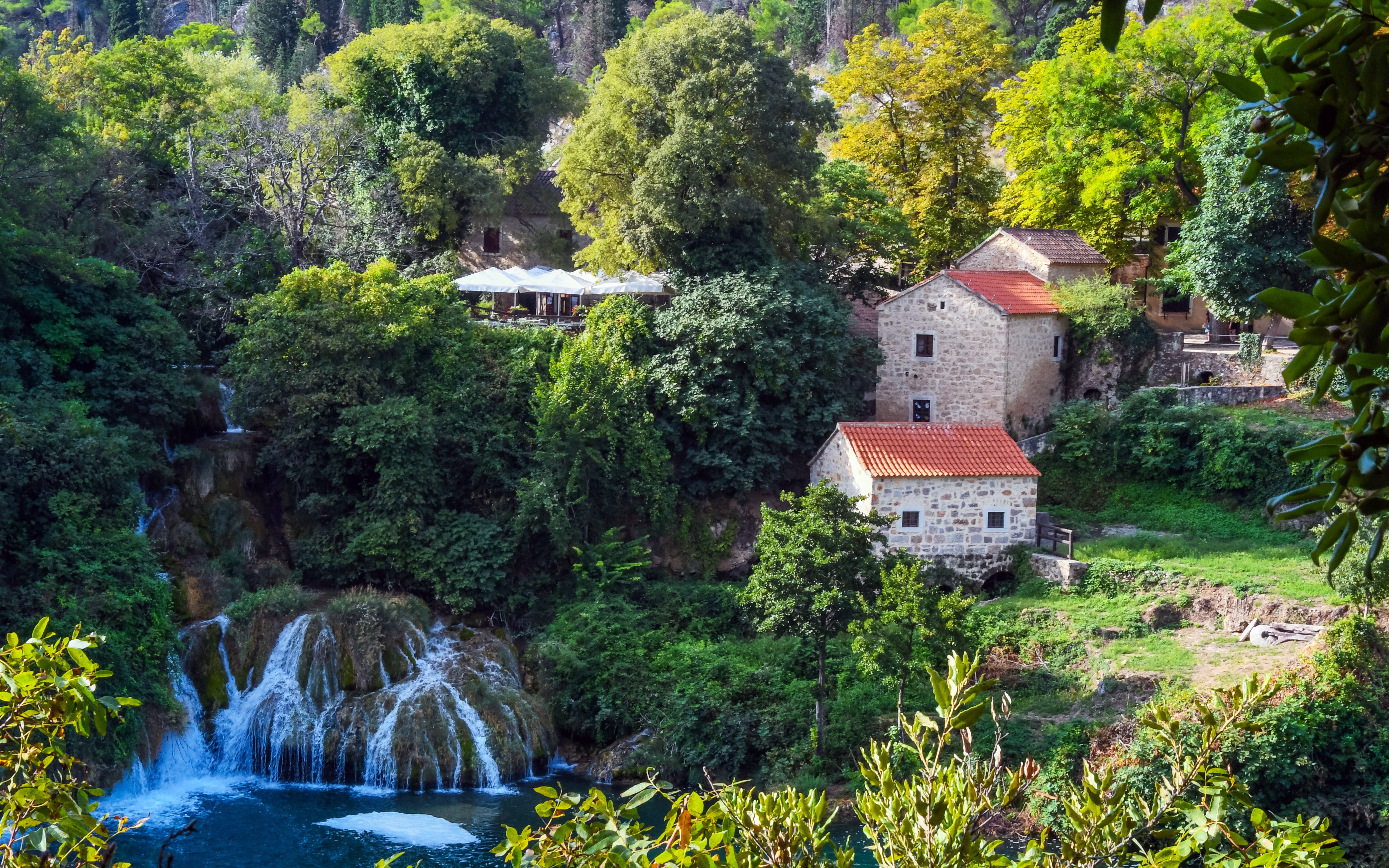 Waterfalls and historic mill buildings surrounded by lush greenery in Krka National Park, Croatia.