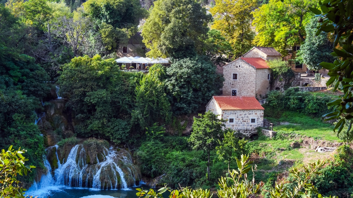 Waterfalls and historic mill buildings surrounded by lush greenery in Krka National Park, Croatia.