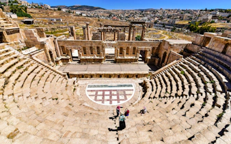 Roman theater in Jerash, Jordan with visitors exploring the ancient stone seating and stage.