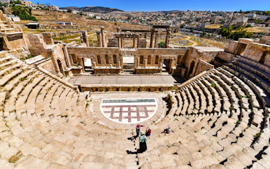 Roman theater in Jerash, Jordan with visitors exploring the ancient stone seating and stage.