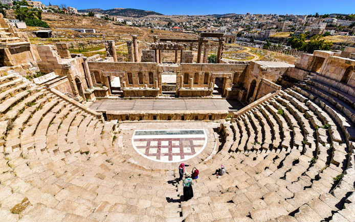 Roman theater in Jerash, Jordan with visitors exploring the ancient stone seating and stage.