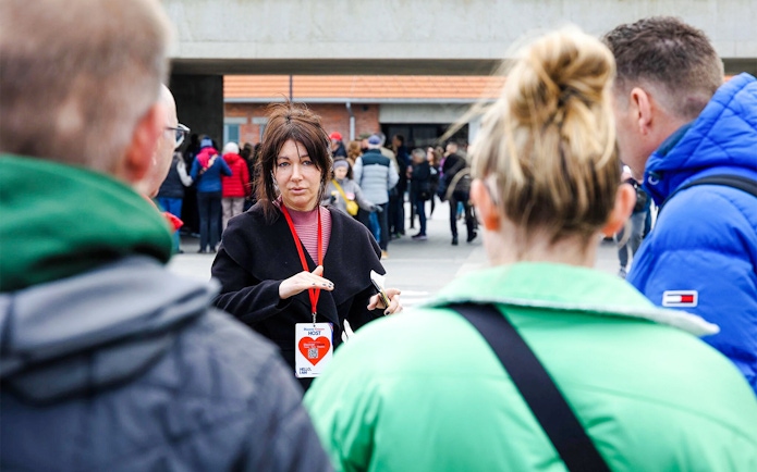 Guide leading Auschwitz-Birkenau tour with group in background.