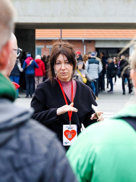 Guide leading Auschwitz-Birkenau tour with group in background.