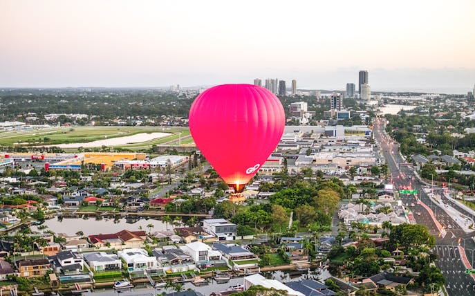Hot air balloon over cityscape with skyline and river in the background.
