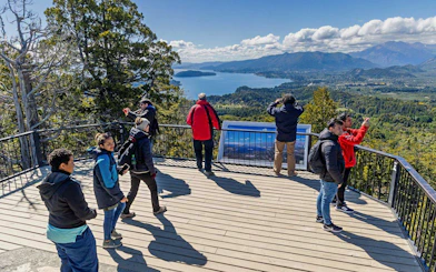 Travelers at a Bariloche viewpoint enjoying views of lakes and mountains.