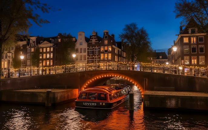 Canal boat under illuminated bridge during Amsterdam Light Festival.