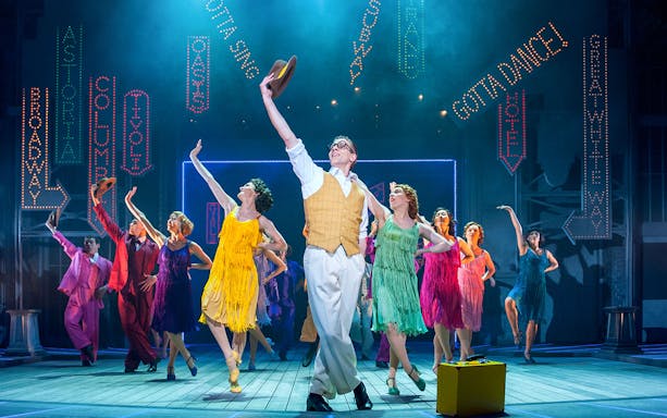 Performers dancing on stage in colorful costumes during Singin’ in the Rain musical.