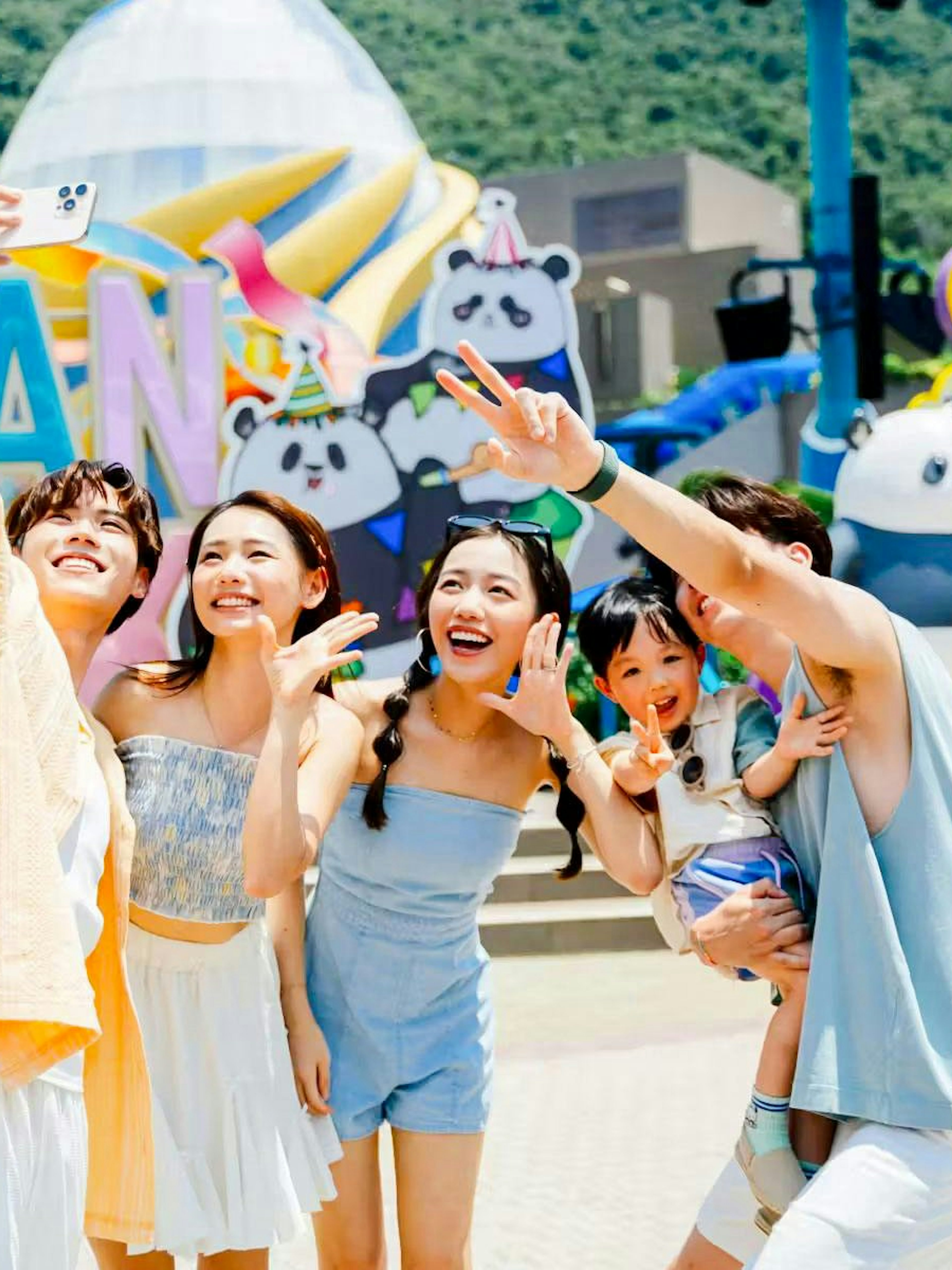 Family taking a selfie at Ocean Park entrance with colorful panda decorations.