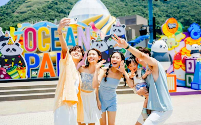 Family taking a selfie at Ocean Park entrance with colorful panda decorations.