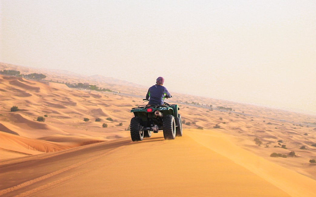 Person riding a quad bike on sand dunes in Abu Dhabi desert.