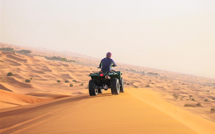 Person riding a quad bike on sand dunes in Abu Dhabi desert.