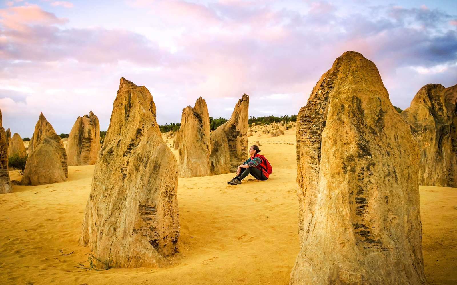 Person sitting among limestone formations at sunset, Pinnacles Desert, Australia.