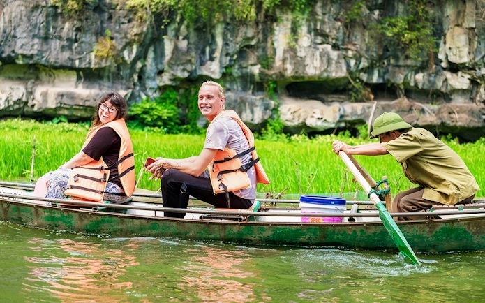 Tourists in a boat on Tam Coc river, Vietnam, with limestone cliffs in the background.
