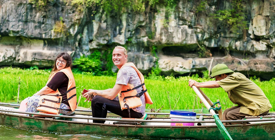 Tourists in a boat on Tam Coc river, Vietnam, with limestone cliffs in the background.