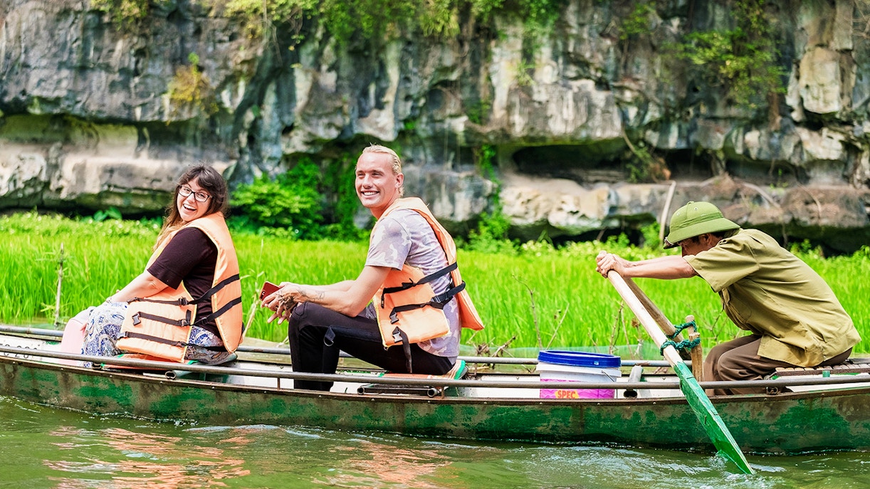 Tourists in a boat on Tam Coc river, Vietnam, with limestone cliffs in the background.