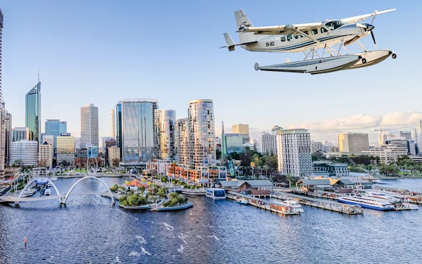Seaplane flying over water with Perth cityscape in the background.