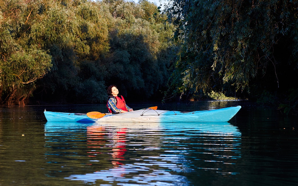 Kayaker relaxing on calm waters surrounded by lush greenery in Blue Eye, Albania.