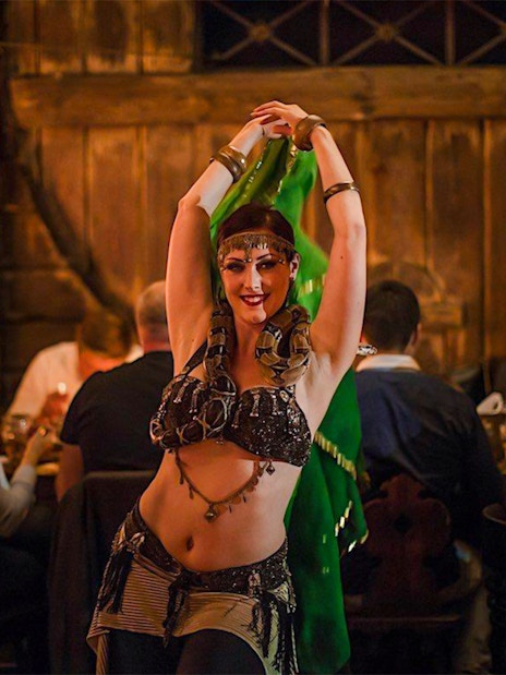 Bellydancer performing at a medieval dinner show with guests dining in the background.