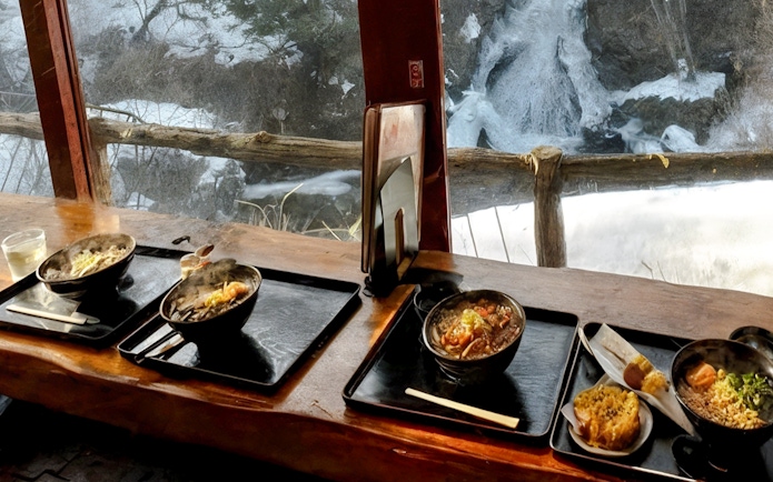 Bowls of steaming noodles on a table at Ryuzu no Chaya, overlooking Ryūzu Falls.