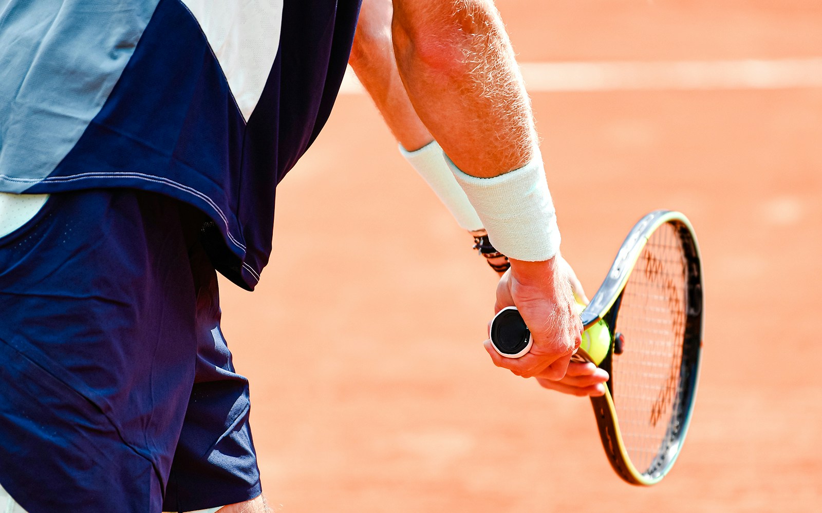 Tennis player preparing to serve on clay court at Roland Garros Stadium.