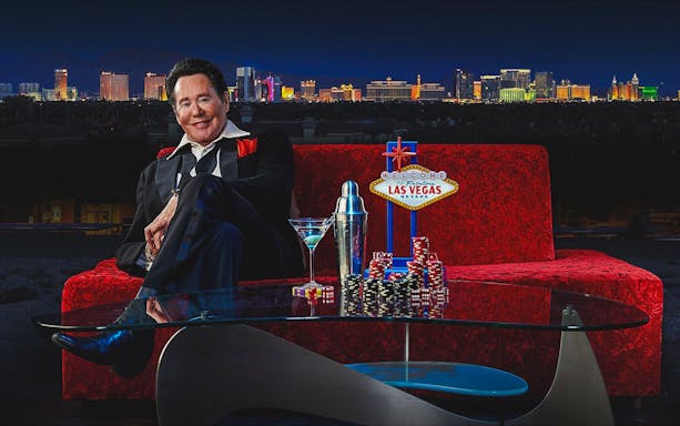 Wayne Newton on red couch with Las Vegas skyline, poker chips, and cocktail.