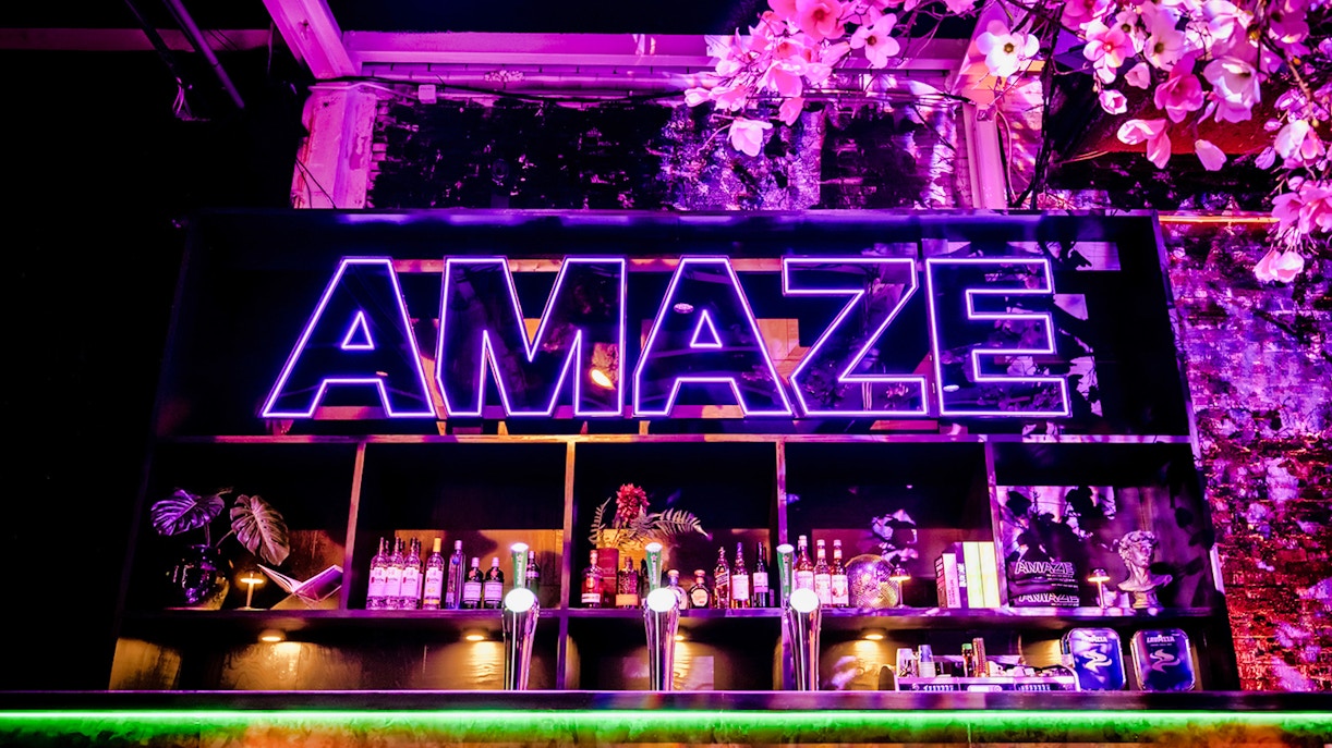 Neon sign at AMAZE Amsterdam with bar and floral decor.