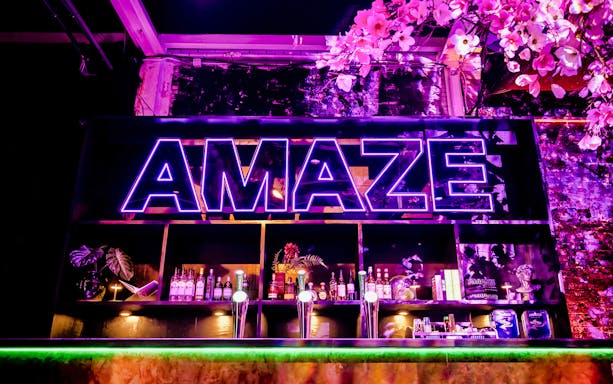 Neon sign at AMAZE Amsterdam with bar and floral decor.