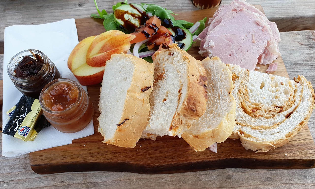 Ploughman's lunch with sliced bread, ham, apple, salad, and chutneys on a wooden board.