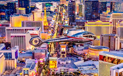 Helicopter flying over the illuminated Las Vegas Strip at night.
