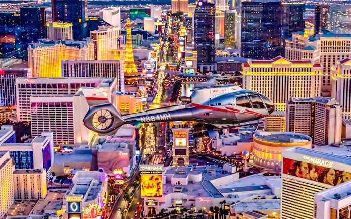 Helicopter flying over the illuminated Las Vegas Strip at night.