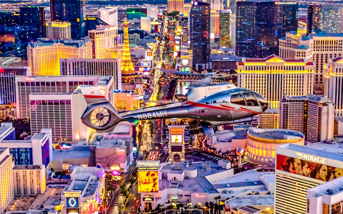 Helicopter flying over the illuminated Las Vegas Strip at night.