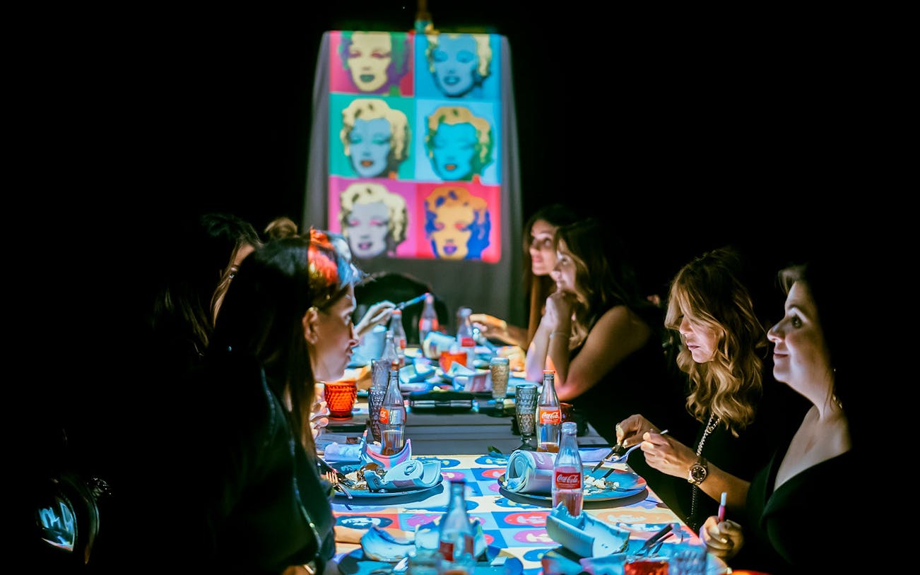 Guests dining at a table with pop art projections during the Seven Paintings Immersive Dining Show.